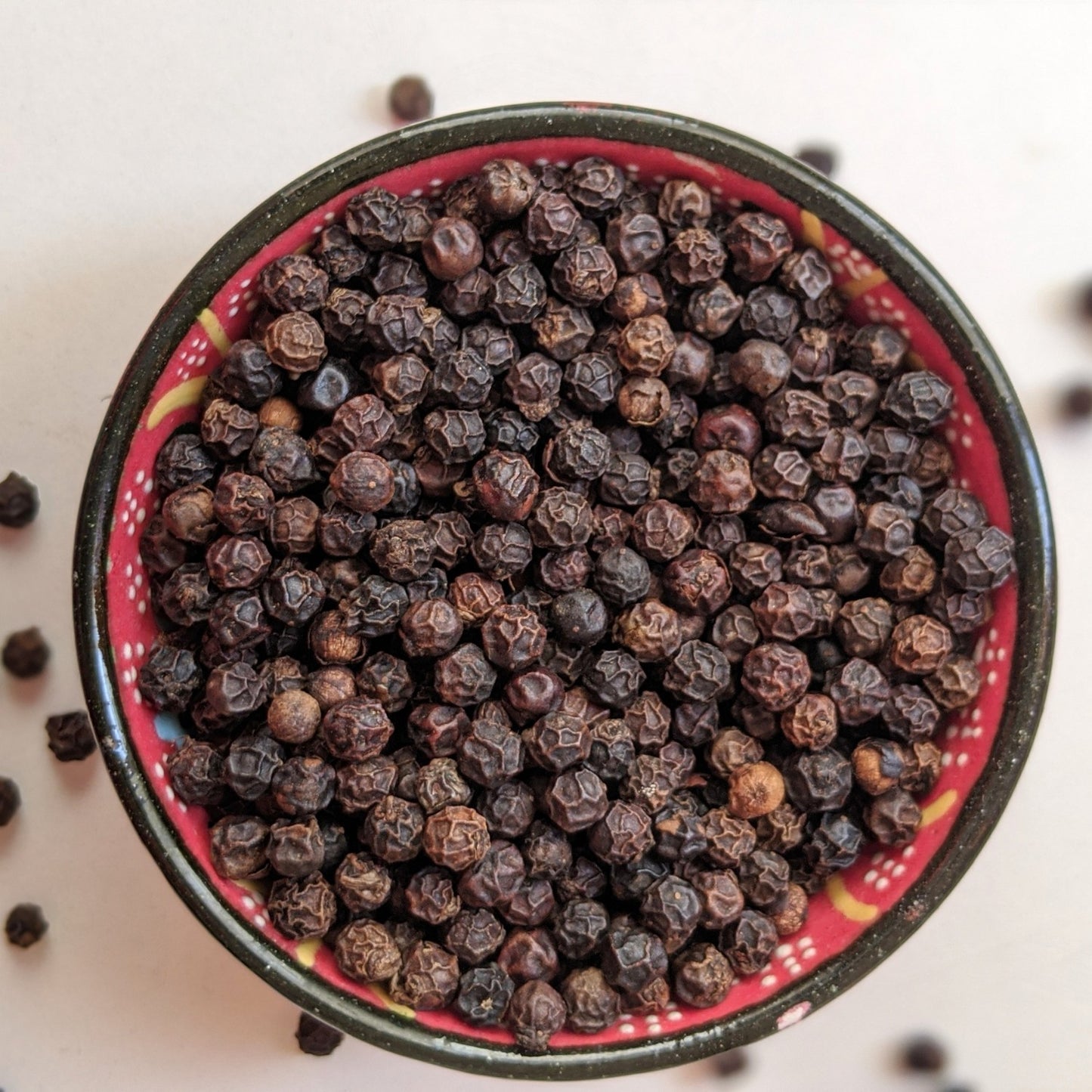 Angadi of Spices whole black peppercorns, TGSEB grade, in a decorative bowl. Bold, aromatic, and rich in essential oils.