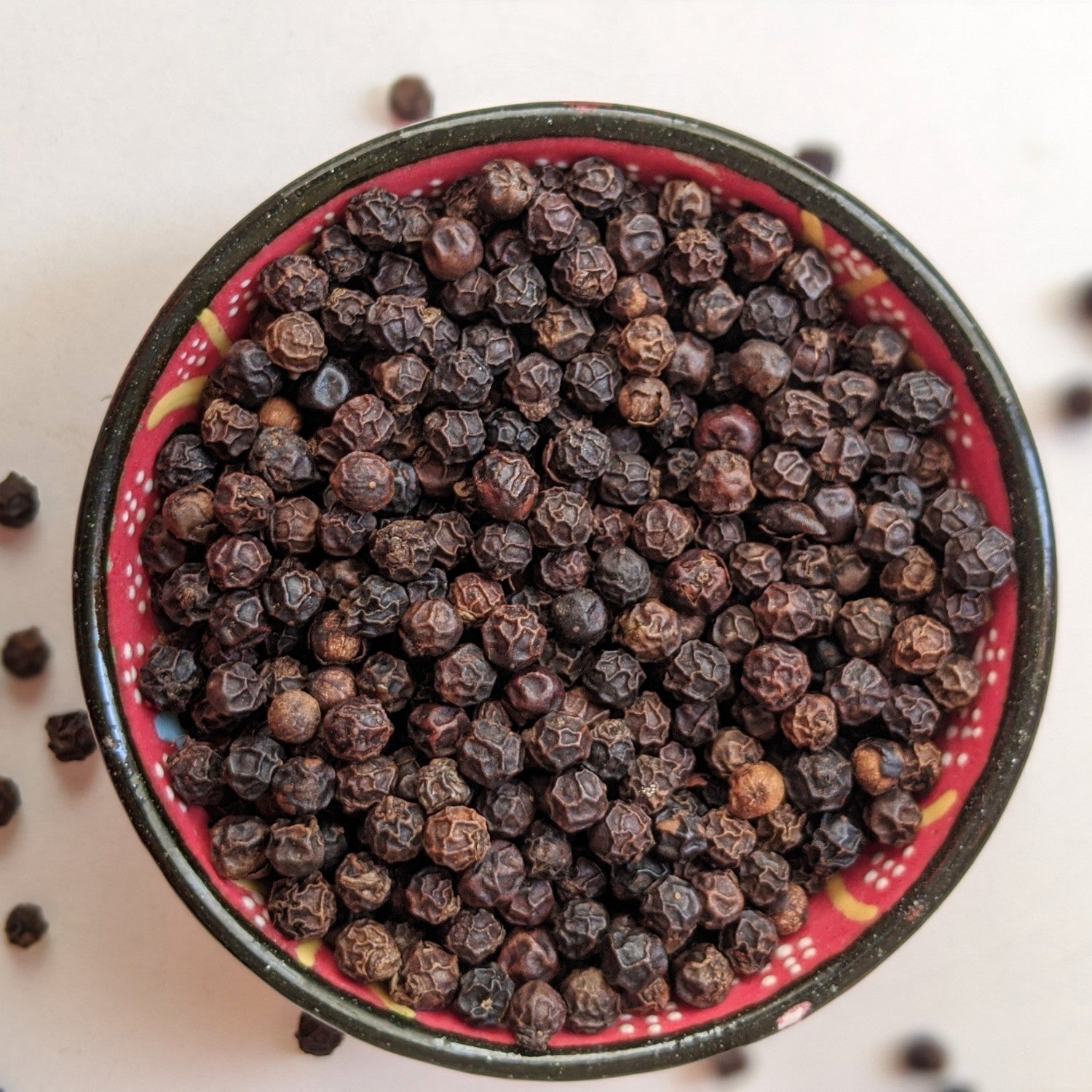 Angadi of Spices whole black peppercorns, TGSEB grade, in a decorative bowl. Bold, aromatic, and rich in essential oils.